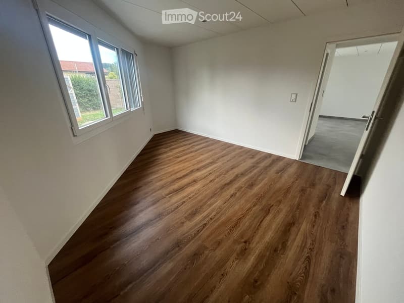 Empty room with wooden flooring, white walls, and large windows letting in natural light. No furniture or equipment is present.