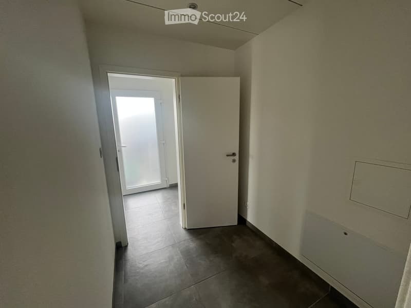 Empty hallway with tiled floor, white walls, and a closed door leading to another room.