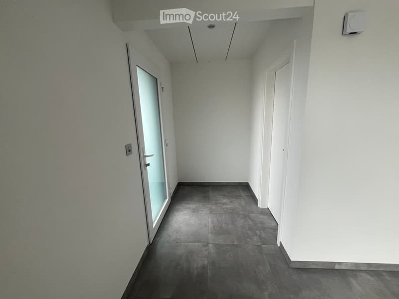 Empty hallway with grey tiled floor, white walls, and two doors (one with a glass panel).