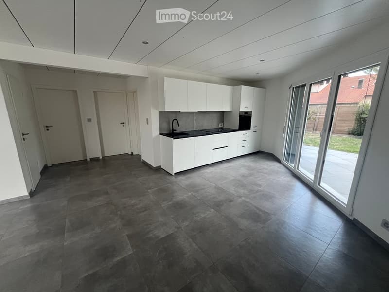 Modern kitchen with white cabinets, dark countertops, and a large window overlooking a garden.