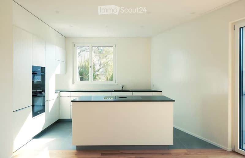 Modern kitchen with white cabinets, a central island, and a window overlooking greenery.