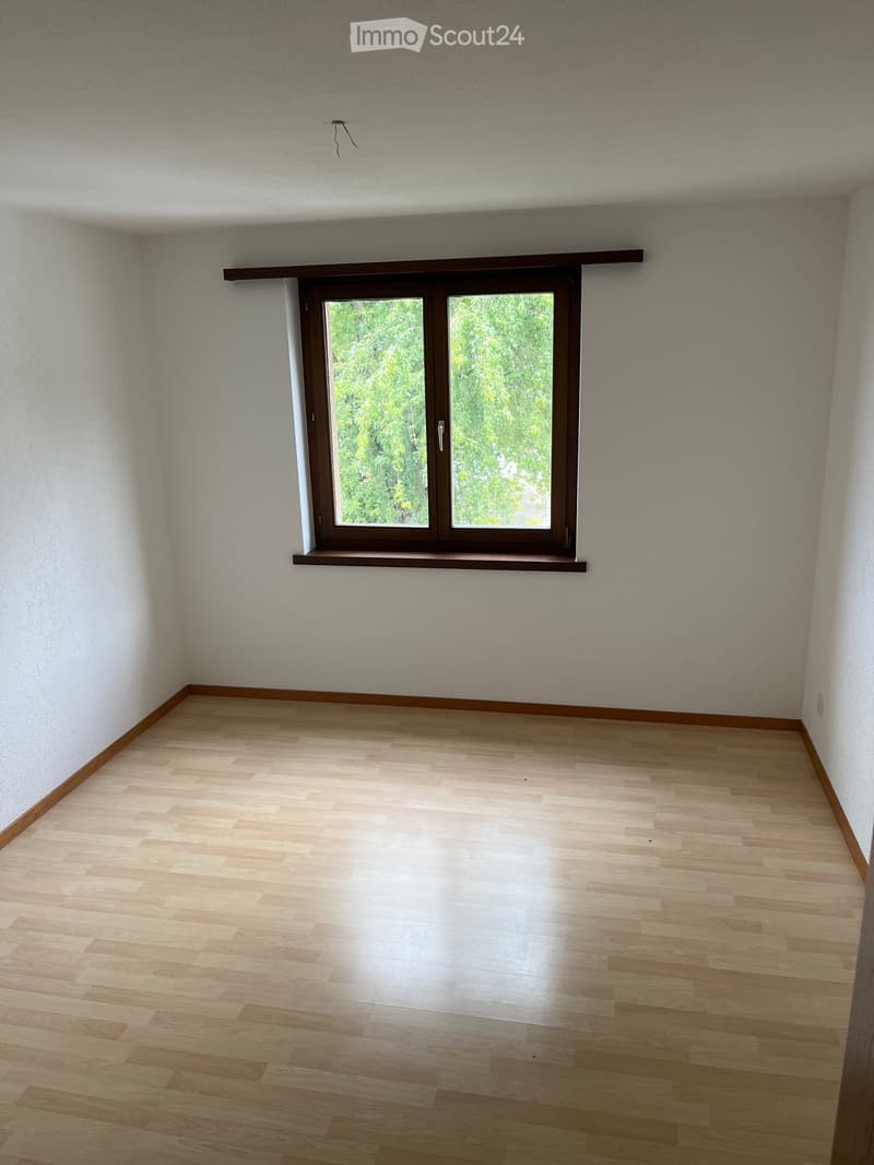 Empty room with light wooden flooring, white walls, and a large window with a wooden frame and sill.