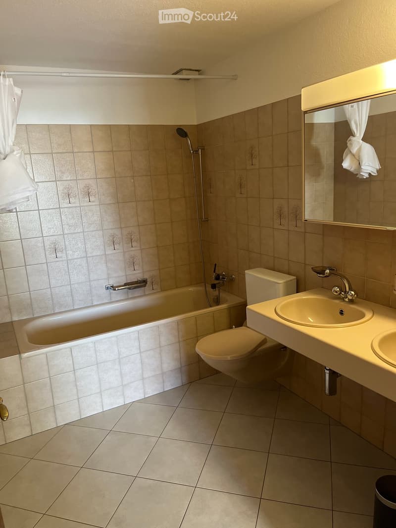 Bathroom with a bathtub, toilet, sink, and mirror. The walls are tiled with a decorative tree pattern, and the floor is tiled with light-colored tiles.