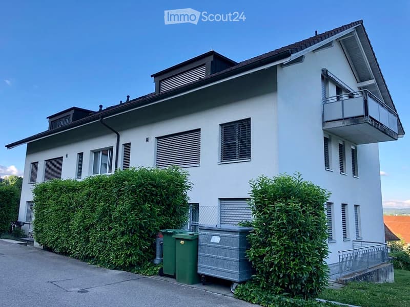 White painted exterior, rectangular windows, small balcony on the top floor, and a fence in front
