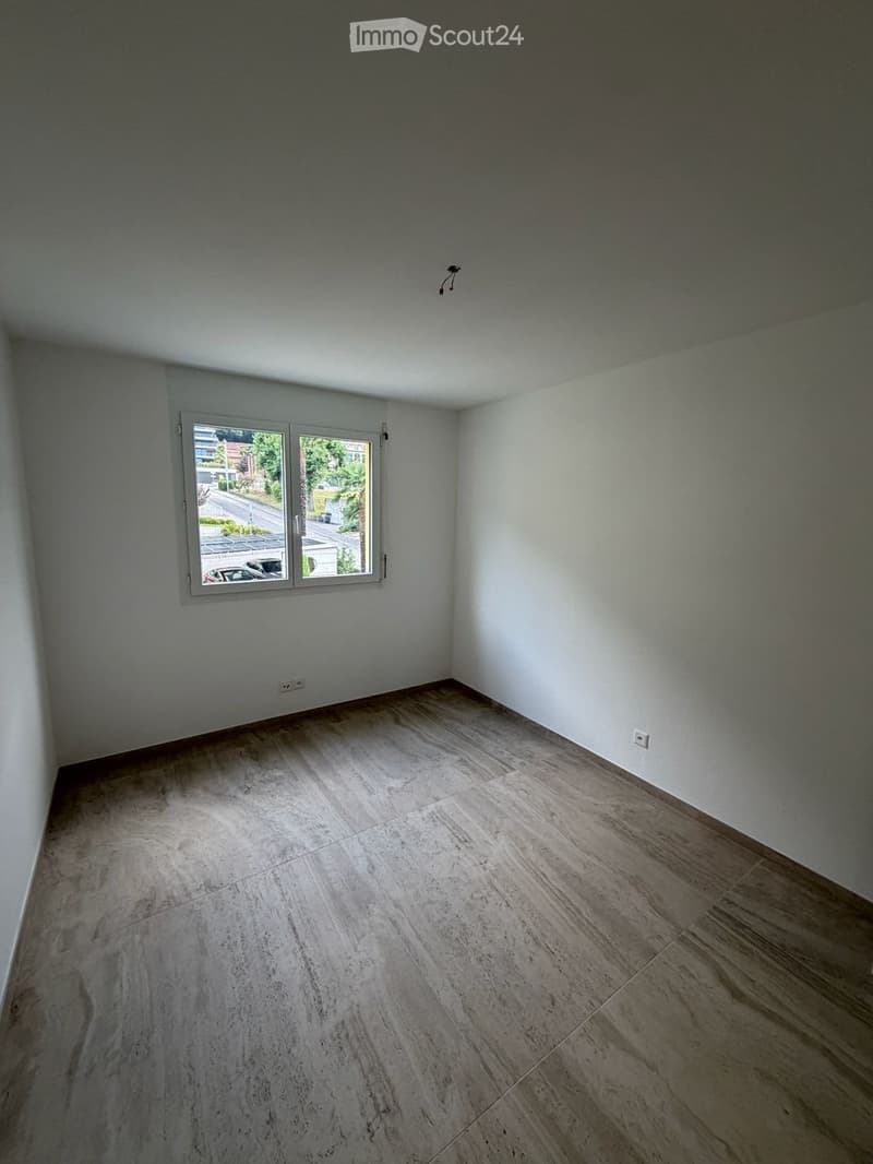 Empty room with light grey walls, large window, and light grey tiled floor.