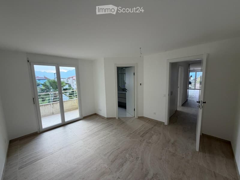 Empty room with light-colored walls, wooden flooring, and large sliding glass doors leading to a balcony with a scenic view.