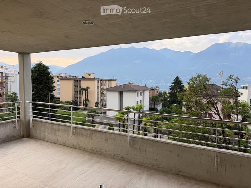 Balcony with a metal railing, concrete floor, and a scenic view of mountains and city buildings.