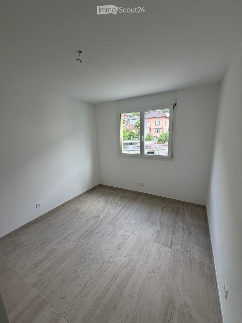 Empty room with light grey walls, wooden floor, and a window showing a view of the outside.