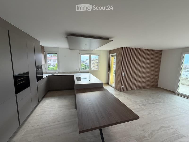 Modern kitchen with grey cabinets, a central island, and a wooden dining table. Large windows and a sliding door lead to a balcony.