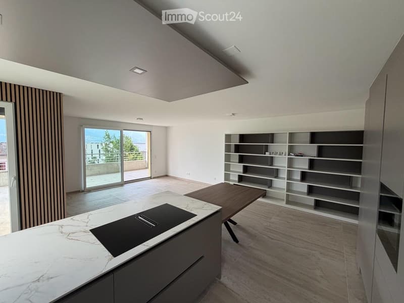 Modern, open-plan kitchen and living area with a marble island, induction cooktop, wooden table, and built-in bookshelf. Large sliding glass doors lead to a balcony.