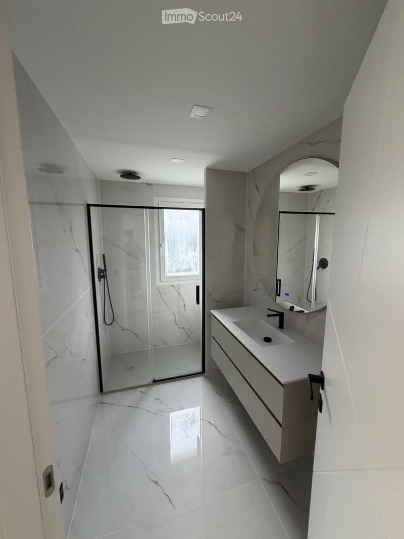 Modern bathroom with white marble tiles, a glass-enclosed shower, a sink with a modern faucet, and a large mirror above the sink.