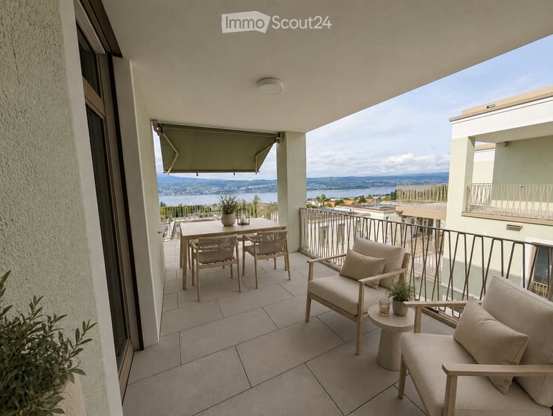 Balcony with a view of a lake and mountains, featuring a sofa, chairs, a table, and potted plants.