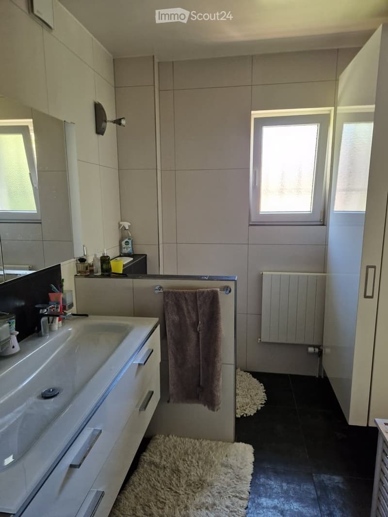 Modern bathroom with a white sink, mirror, towel, radiator, and a small window letting in natural light.