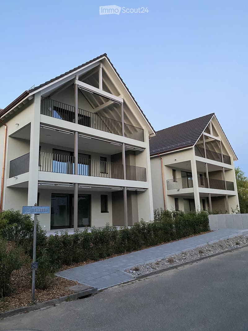 Two-story residential building with balconies, modern design, and a sloped roof.