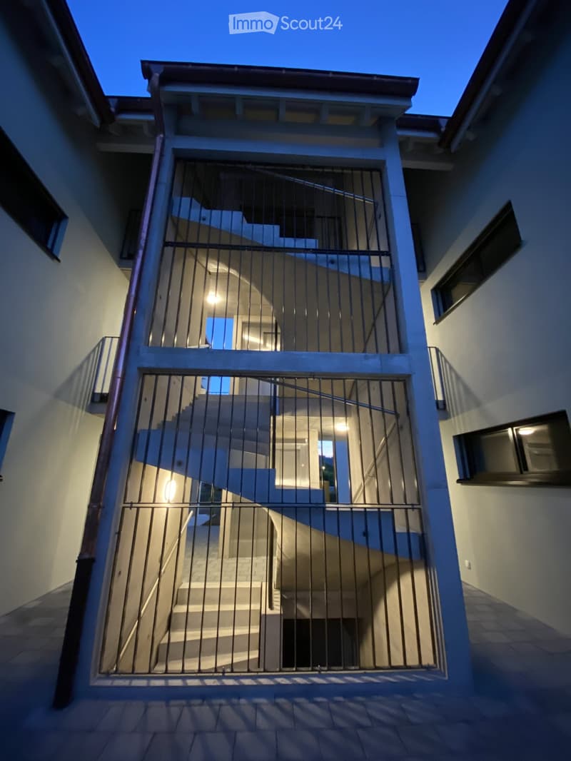 Modern two-story building with a curved staircase and metal railing, illuminated at night.
