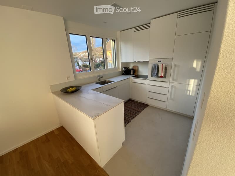 Modern kitchen with white cabinets, marble countertop, sink, oven, coffee maker, and a bowl of fruit on the counter.