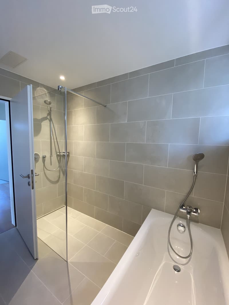 Modern bathroom with a bathtub, glass-enclosed shower, and grey tiles.