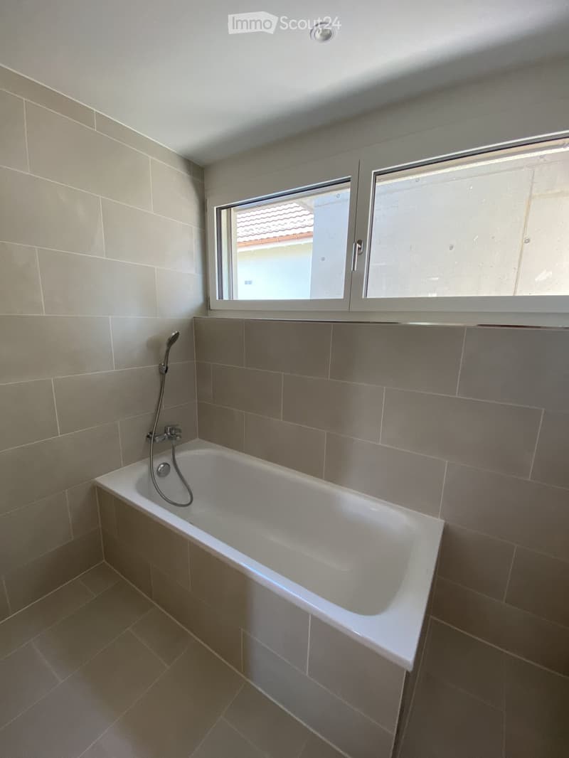 Modern bathroom with a white bathtub, tiled walls, and a window above the tub.
