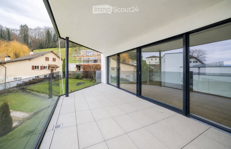 Modern balcony with large glass sliding doors, white tiled floor, and a view of a landscaped garden and neighboring houses.