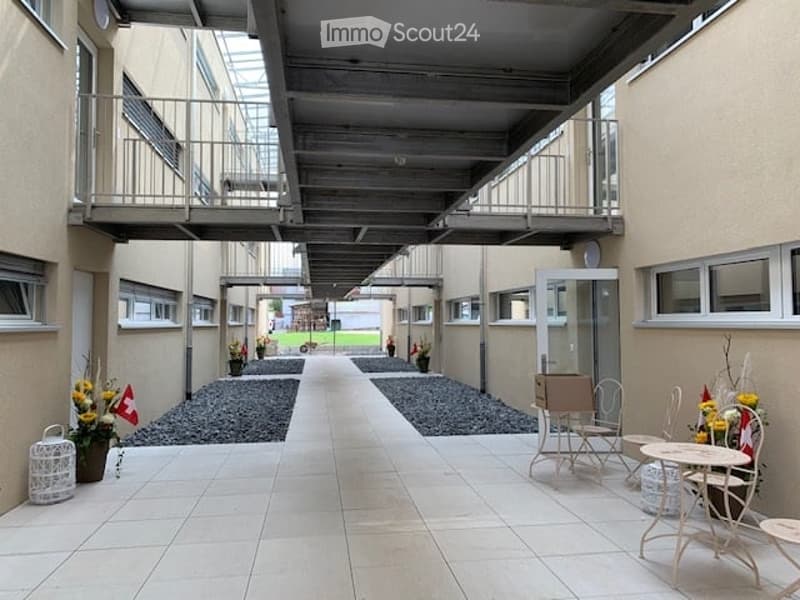 Courtyard area with tiled flooring, gravel pathways, and outdoor furniture including tables and chairs. Potted plants and a small decorative structure are visible.