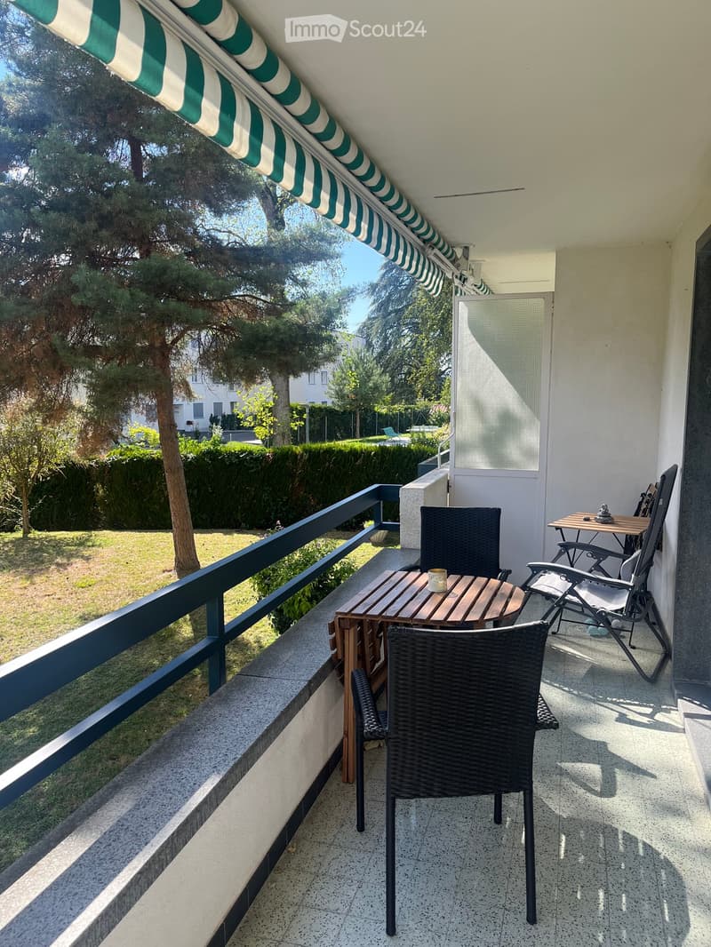 Balcony with a wooden table, wicker chairs, and a green and white striped awning.