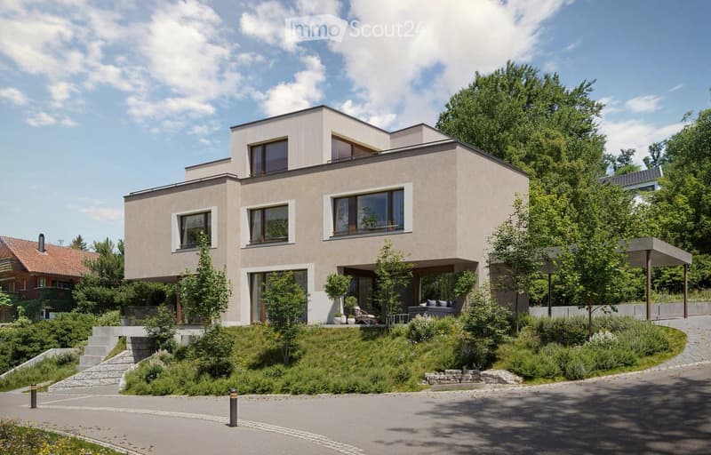 Modern two-story house with raised ground floor, beige exterior, multiple windows, a front driveway, and a small garden area
