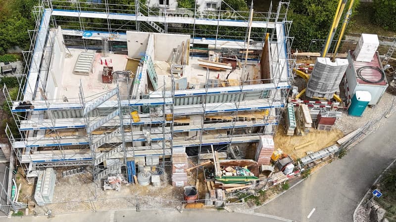 A multi-story building under construction with scaffolding, exposed steel beams, and construction materials scattered around the site.