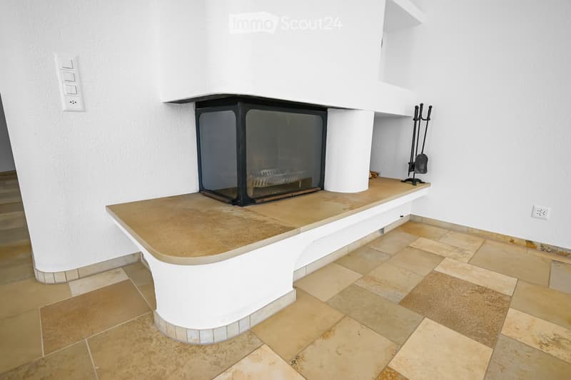 Modern fireplace with a sleek black frame and glass front, placed on a tiled platform with beige tiles and a white curved base.