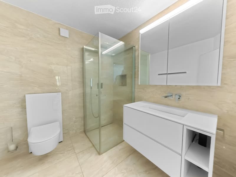 Modern bathroom with white fixtures, a glass-enclosed shower, a toilet, a sink with a mirrored cabinet, and beige tiled walls and floor.