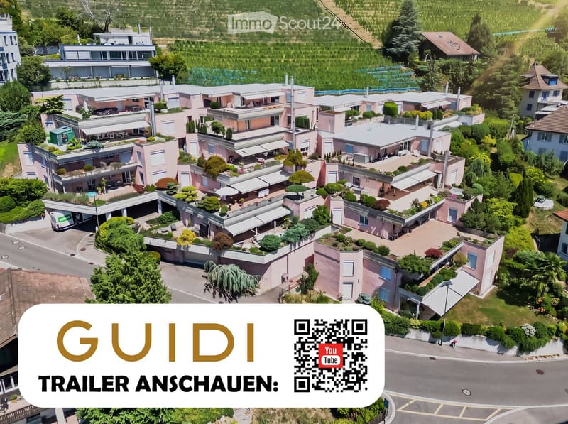 Aerial view of a large residential complex with multiple pink buildings, green gardens, terraces, and a swimming pool.
