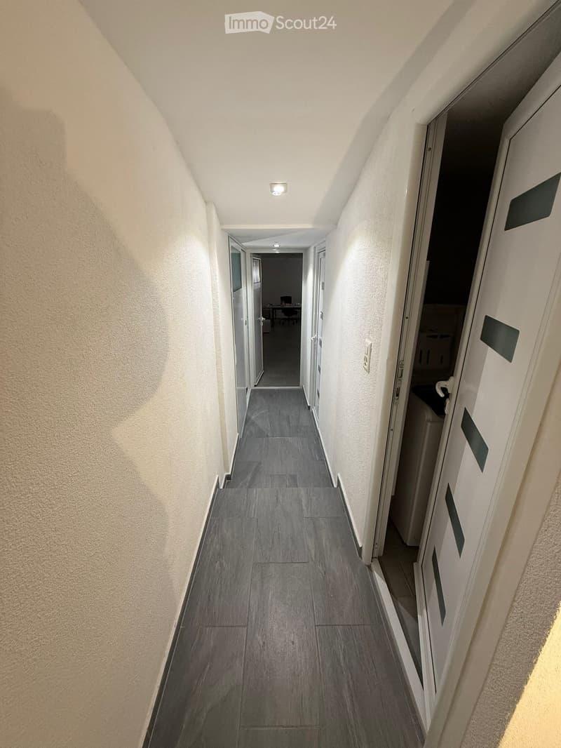 empty corridor with a tiled floor, white walls, two doors on each side, one with a washing machine inside