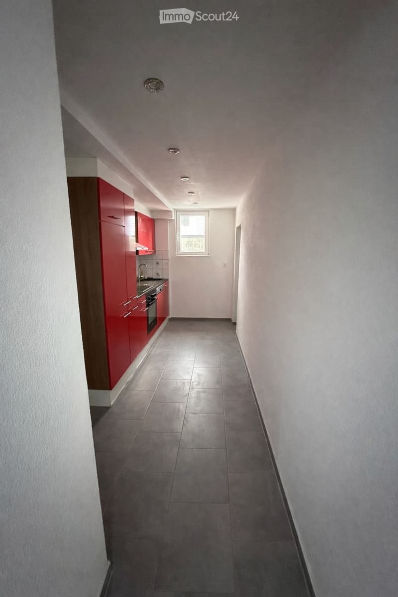 Long hallway, white walls, tile floor, cabinets, countertop, sink, stove, window with city view