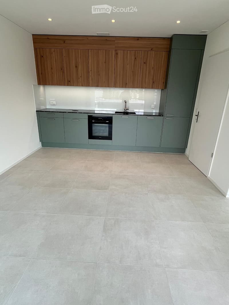 Empty kitchen with modern wooden cabinets, stainless steel appliances, and tiled flooring.