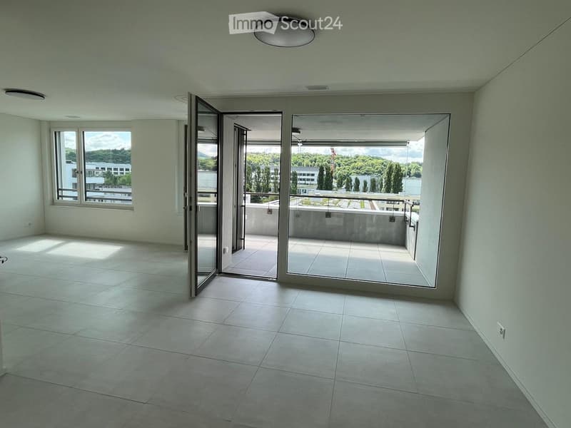 Empty room with tiled floor, large windows, and sliding glass doors leading to a balcony with a view of greenery and buildings.