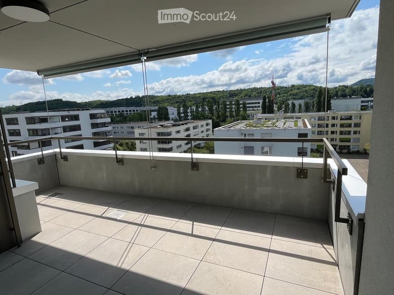 Modern balcony with tiled floor, metal railing, and retractable awning, overlooking a cityscape with buildings and greenery.