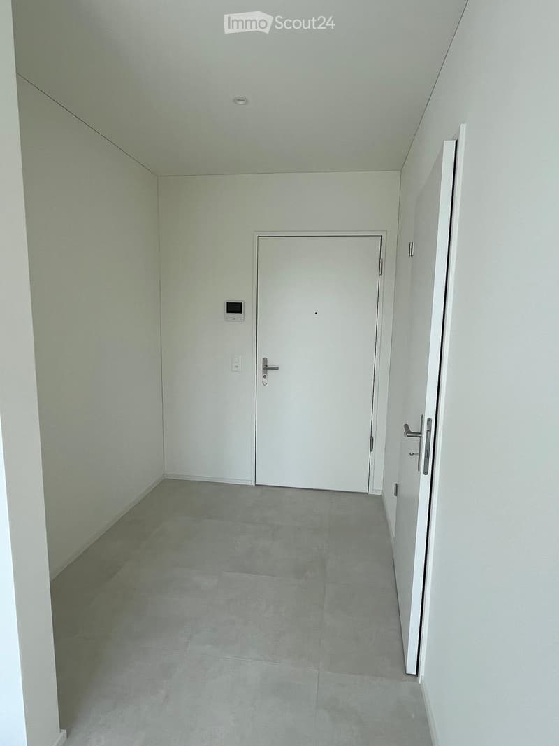 Empty hallway with white walls, grey tiled floor, and a closed white door at the end.
