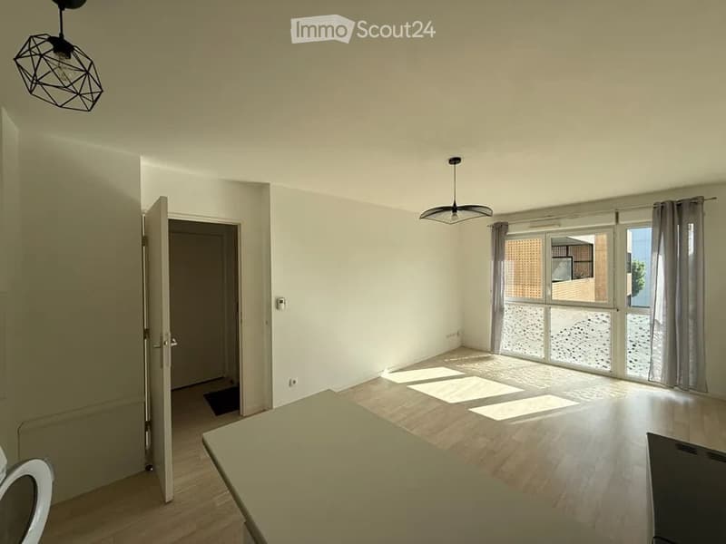Empty room with wooden flooring, white walls, large windows with curtains, and modern pendant lights.