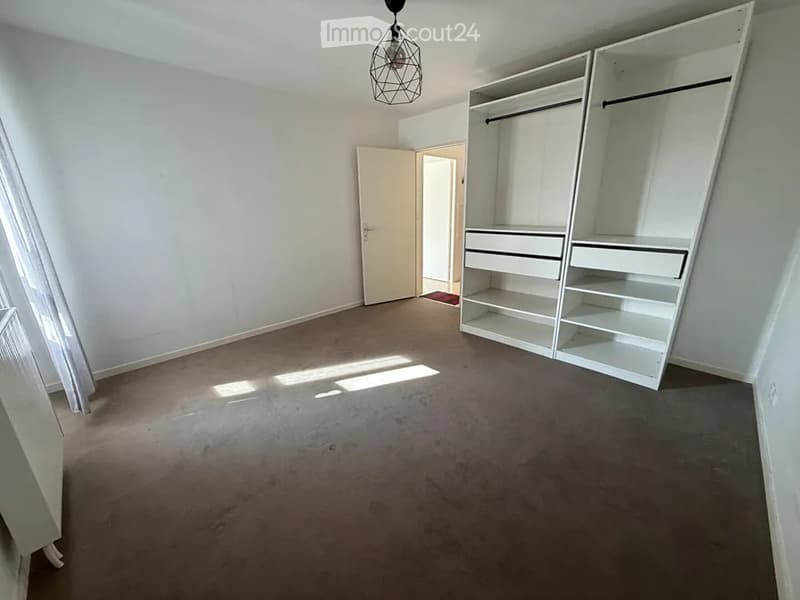Empty room with white walls, carpeted floor, built-in white wardrobe with shelves and drawers, and a hanging light fixture.