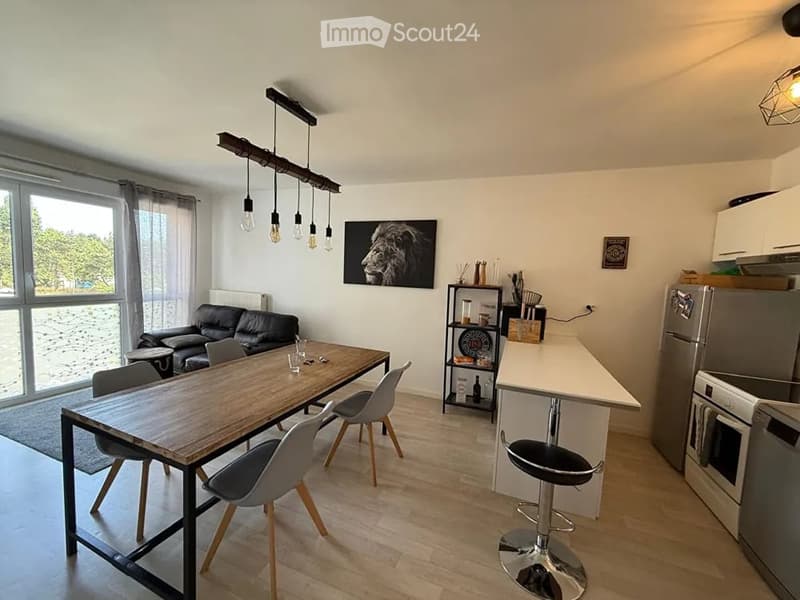 Open-plan living and dining area with a black leather sofa, wooden dining table with chairs, modern kitchen appliances, and pendant lighting.