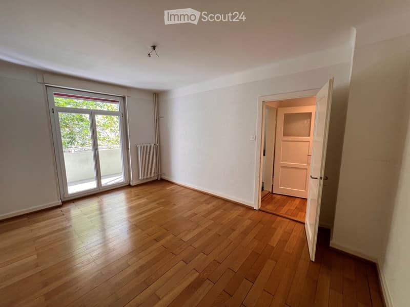 Empty room with wooden flooring, white walls, large sliding glass door, radiator, and an open doorway leading to another room.