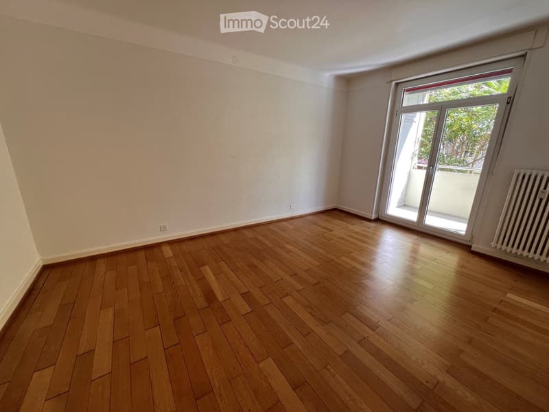 Empty room with wooden flooring, white walls, and a large sliding glass door leading to a balcony.