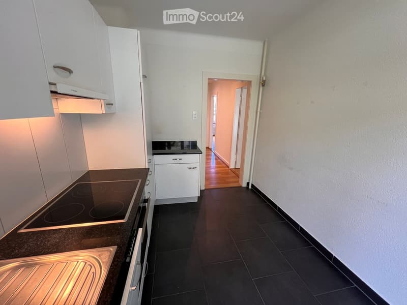 Modern kitchen with white cabinets, black countertop, induction stove, and a sink. The floor is dark tiled, and the walls are light-colored.