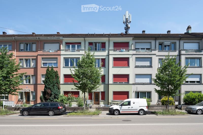 A row of multi-story residential buildings with colorful facades, multiple windows, balconies, and a small garden area in front.