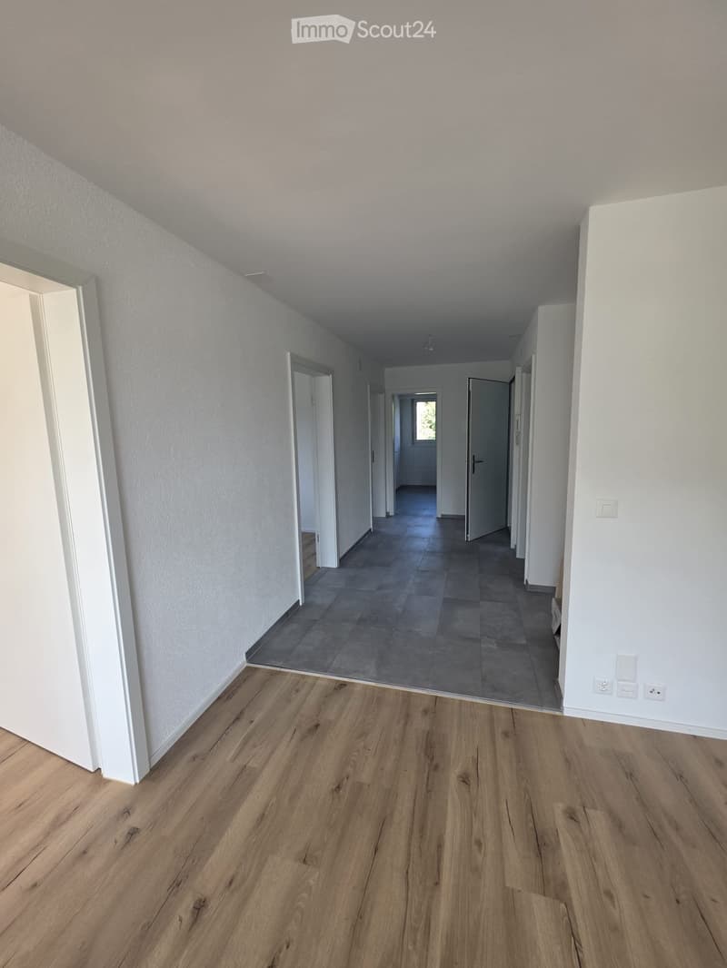 Empty hallway with wooden flooring and white walls, featuring multiple doors leading to other rooms.