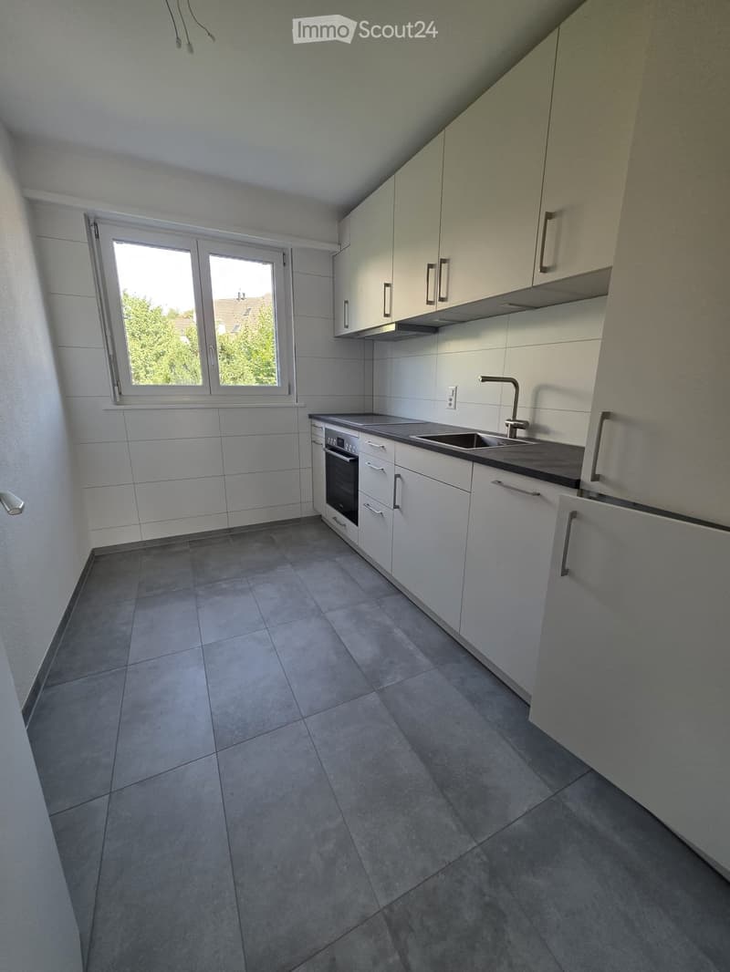 Empty kitchen with white cabinets, stainless steel sink, and tiled floor. No appliances or furniture present.