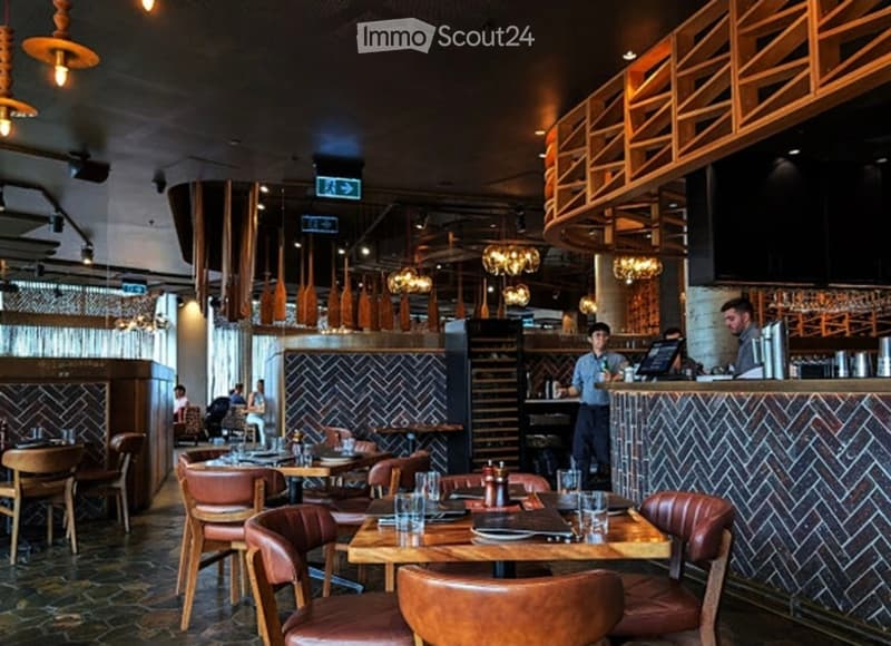 Restaurant interior with wooden tables, leather chairs, bar counter, pendant lights, and wine rack.