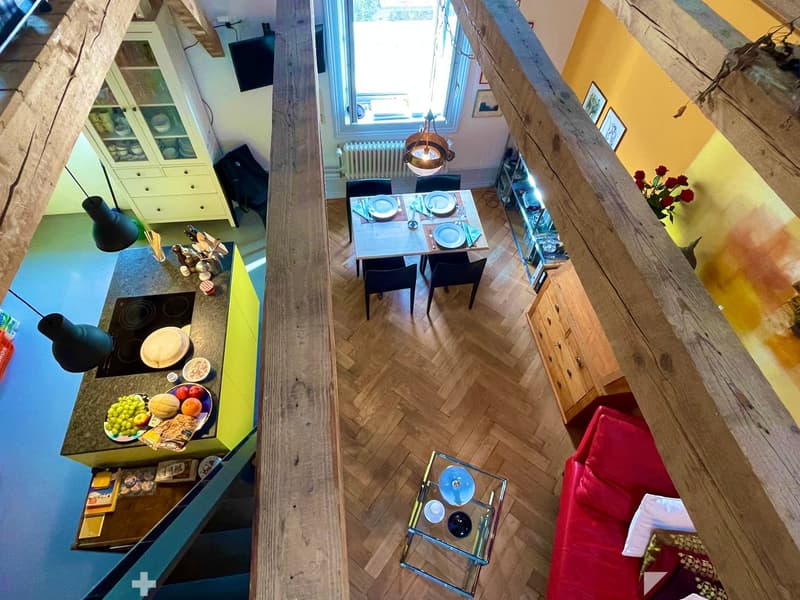 Open-plan living and dining area with a red sofa, glass coffee table, dining table with chairs, kitchen island with induction stove, and pendant lighting.