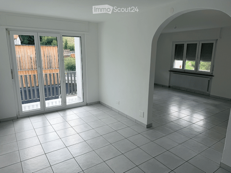 Empty room with tiled floor, white walls, large sliding glass doors leading to a balcony, and a radiator under a window.