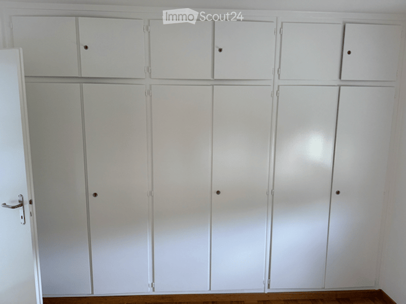 Empty room with white built-in wardrobes and wooden flooring.