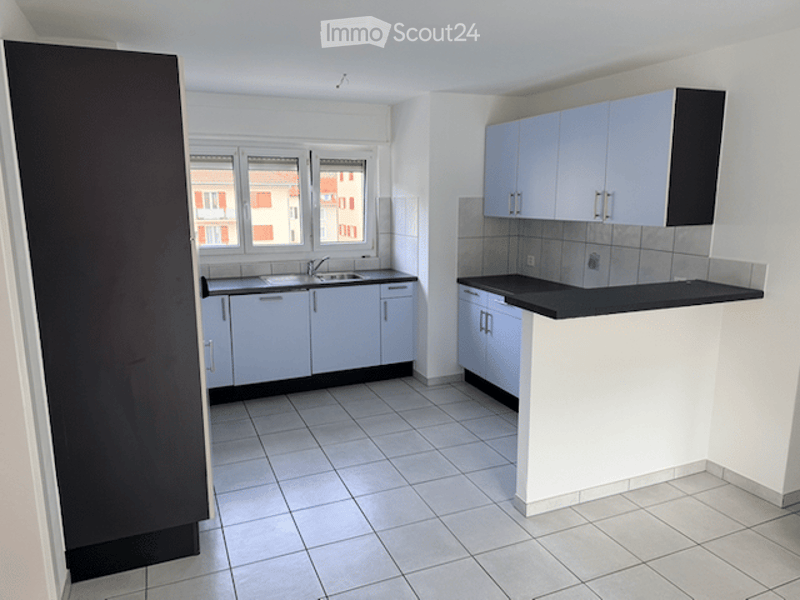 Modern kitchen with white tiled flooring, white cabinets, and a black countertop. Features a sink with a faucet and a window overlooking a red-brick building.
